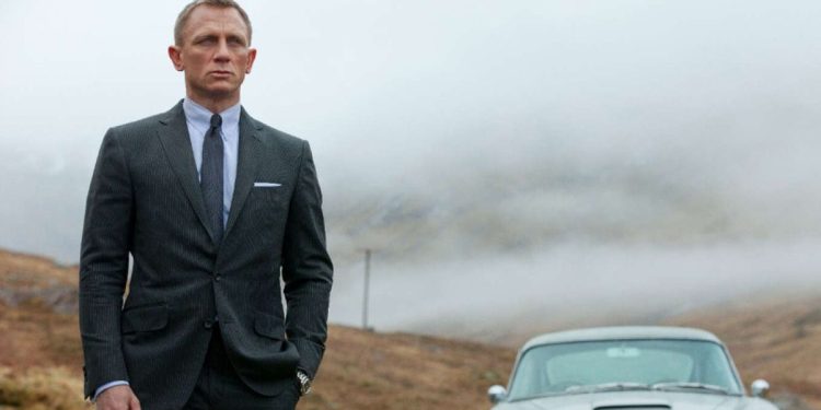 James Bond (Daniel Craig) observa a paisagem de sua antiga casa de infância. Atrás dele, seu famoso carro.